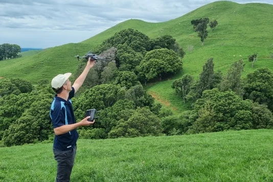 image of man holding a survey drone in lush green field with hill